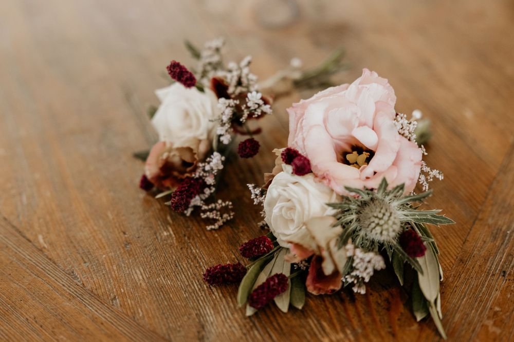 Delicate corsages with pink and white flowers arranged on wooden surface.