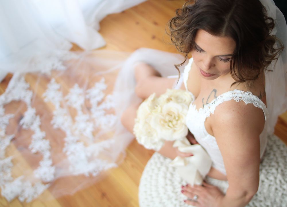 Elegant bridal boudoir photo with cream roses and flowing tulle on wooden floor.