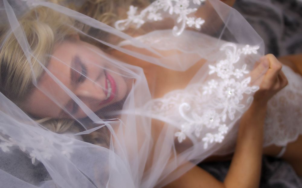Person under delicate lace veil in soft lighting.