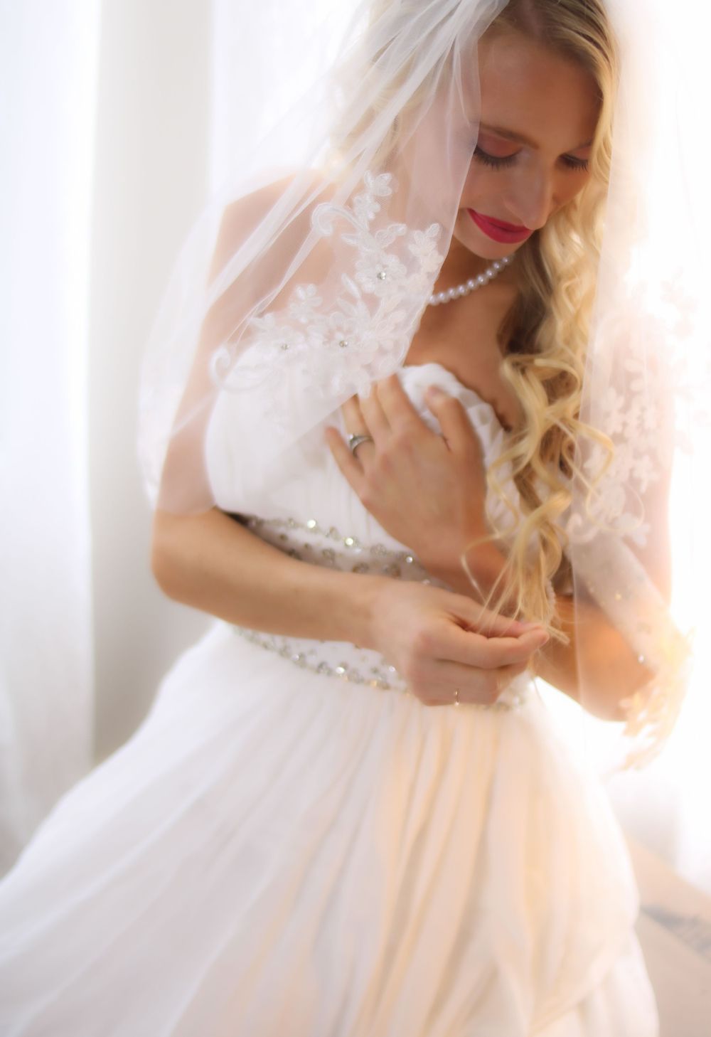 Person in white wedding dress with pearl necklace and lace veil.