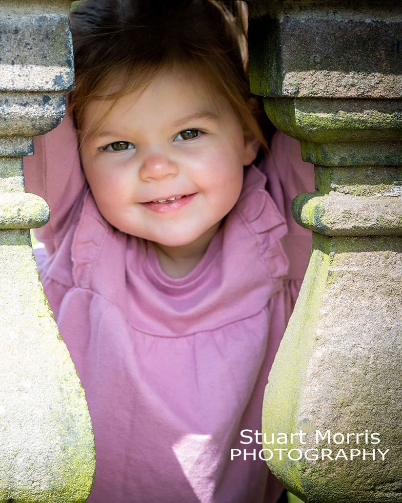 little girl peeps through the stone balustrade at Walton hall garden. outdoor photo session by Stuart Morris Photography