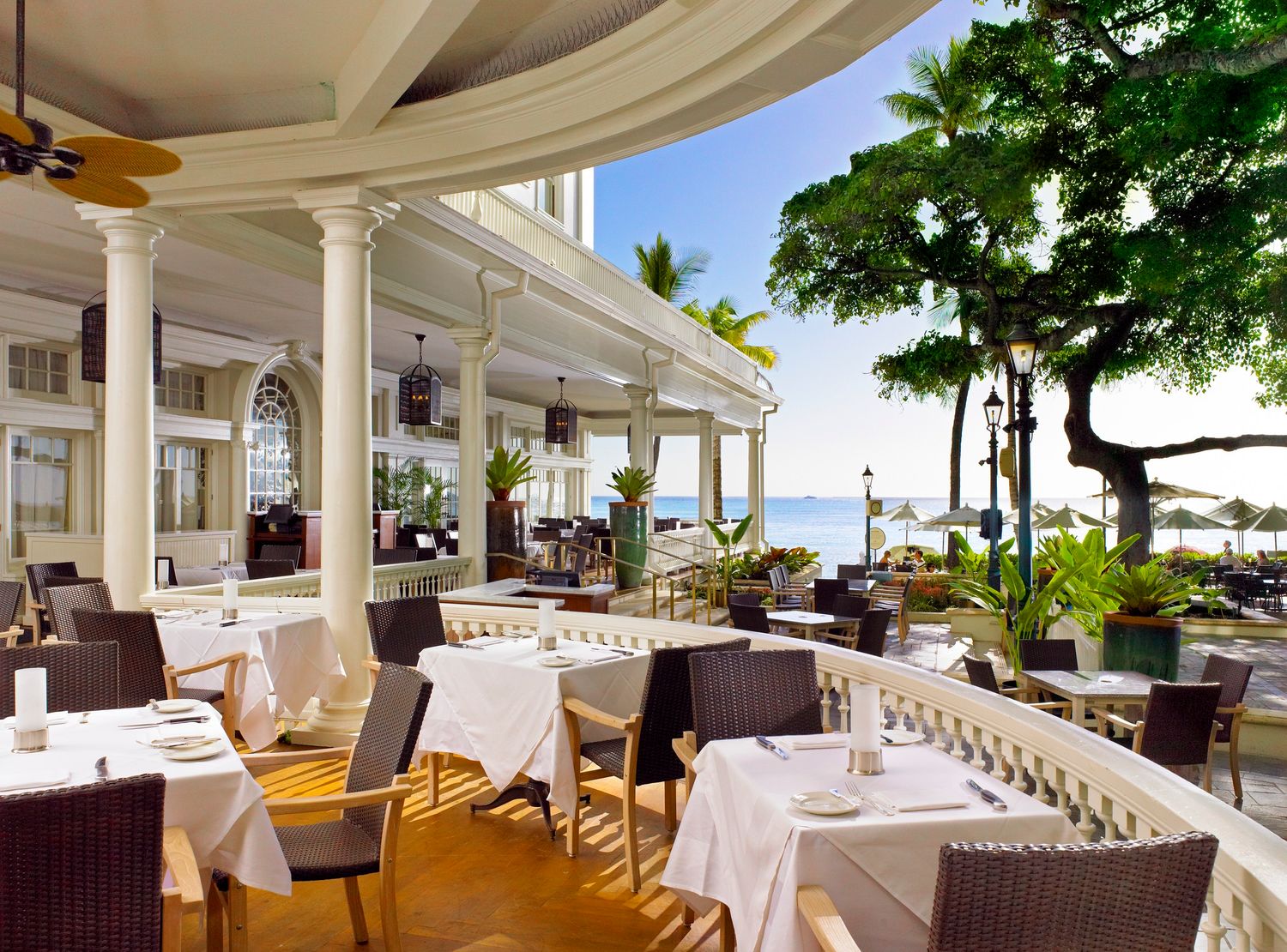 Elegant oceanfront restaurant terrace with white tablecloths, columns, and tropical sea views.