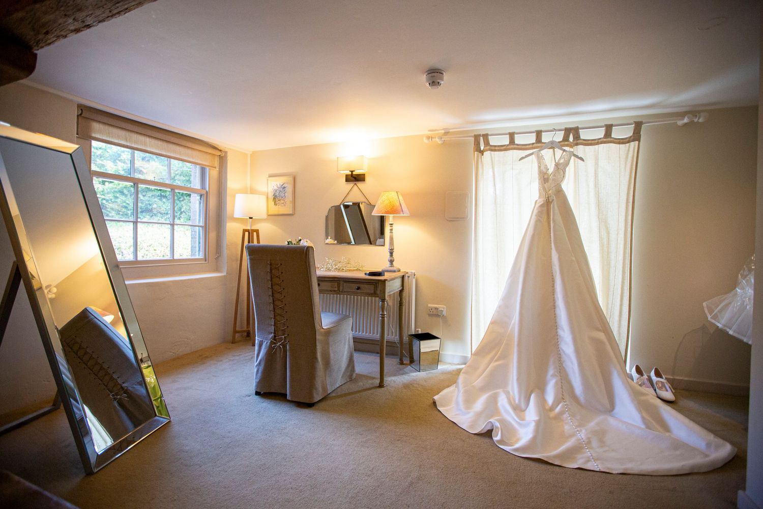 A wedding dress hangs elegantly in a dressing room with natural light and full-length mirrors.