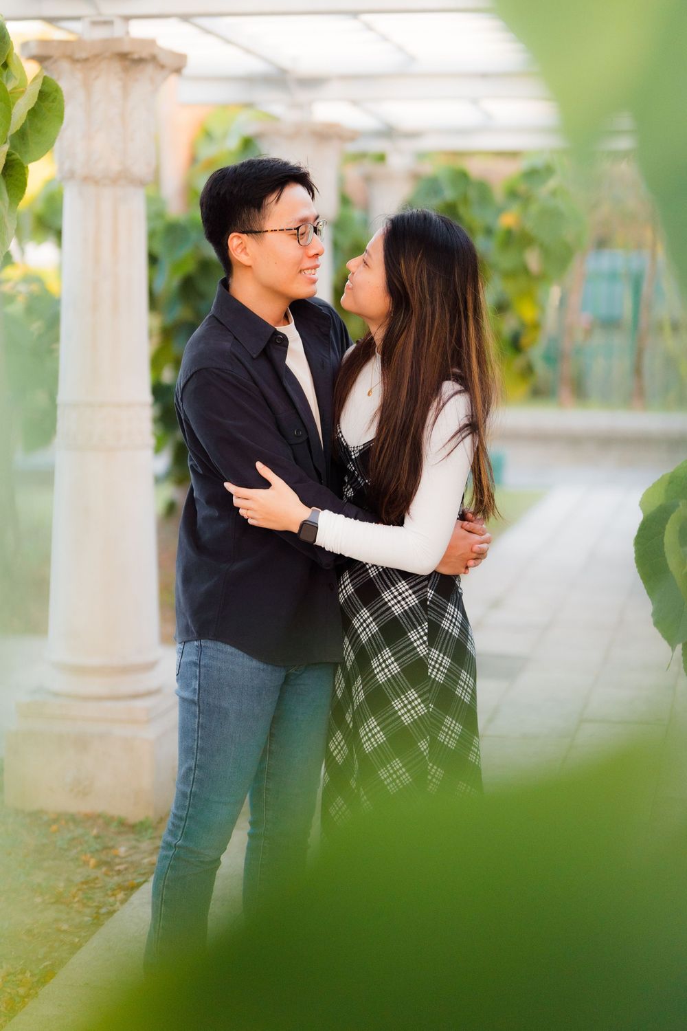 A couple sharing an intimate moment under a white pergola in a lush garden setting.