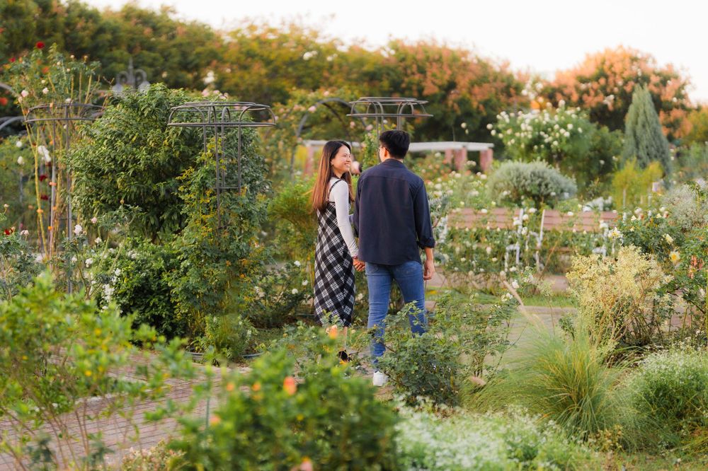 A couple walks together through a lush garden path filled with flowers and greenery.