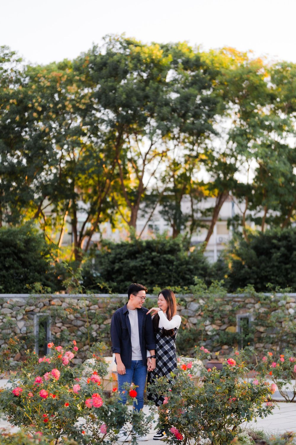 A couple shares a moment together in a garden with stone walls and blooming roses.