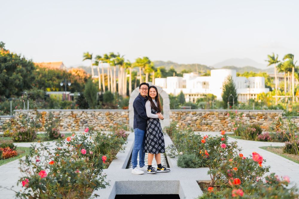 A couple posing together on a platform in a beautiful rose garden with palm trees in the background.
