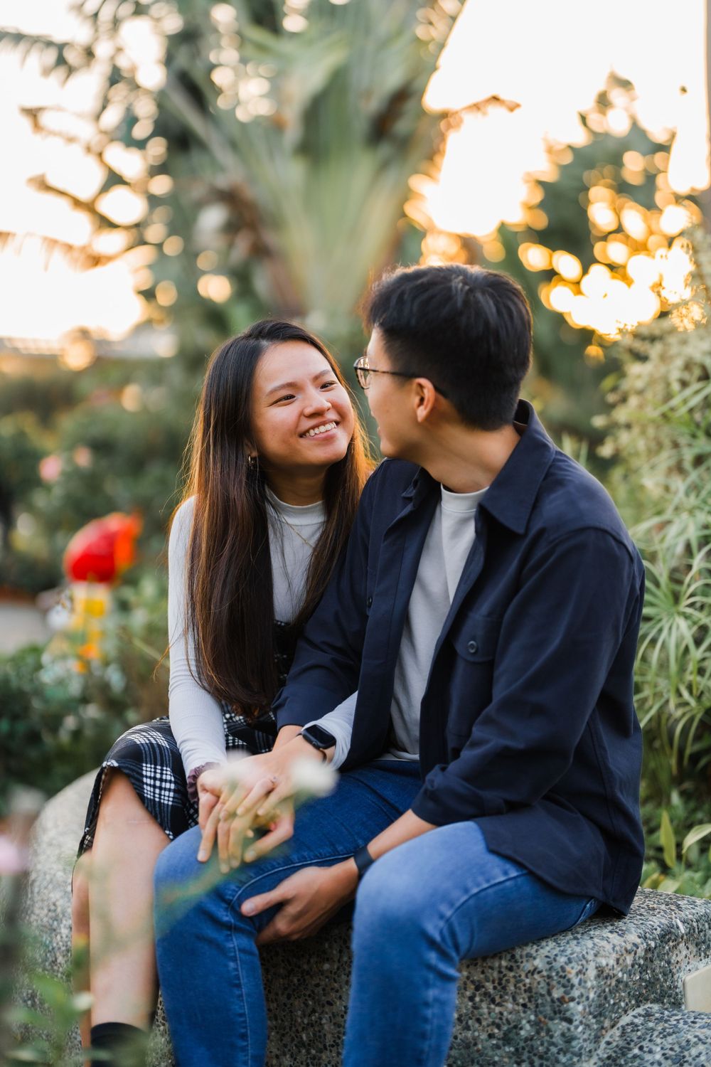 A couple shares a tender moment while sitting in a garden at sunset.