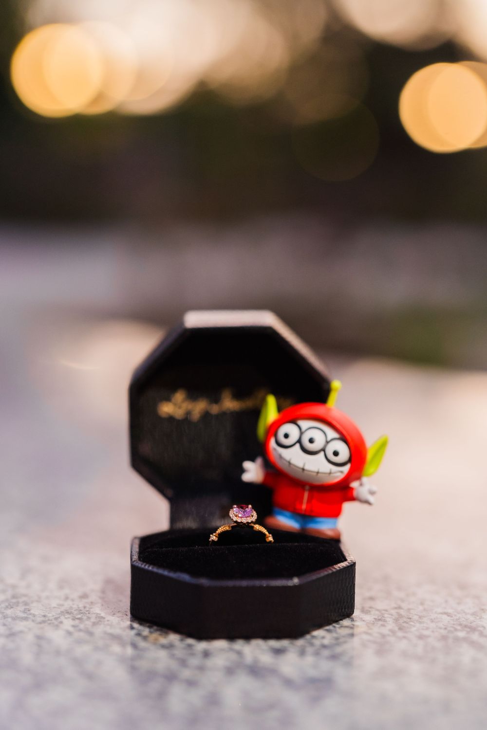 Engagement ring in black box with cute toy minion figure decoration.