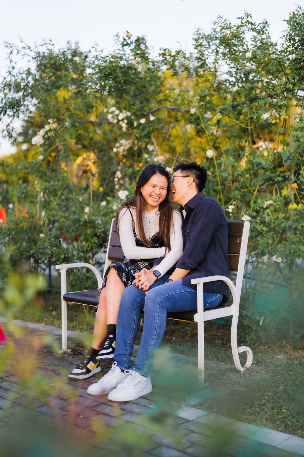 A couple sitting close together on a white bench in a garden with blooming yellow flowers.