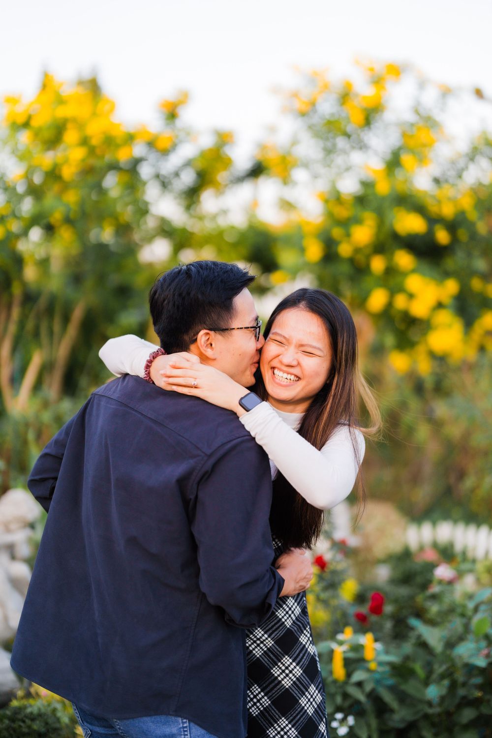 A romantic couple embracing in a garden with yellow flowers blooming in the background.