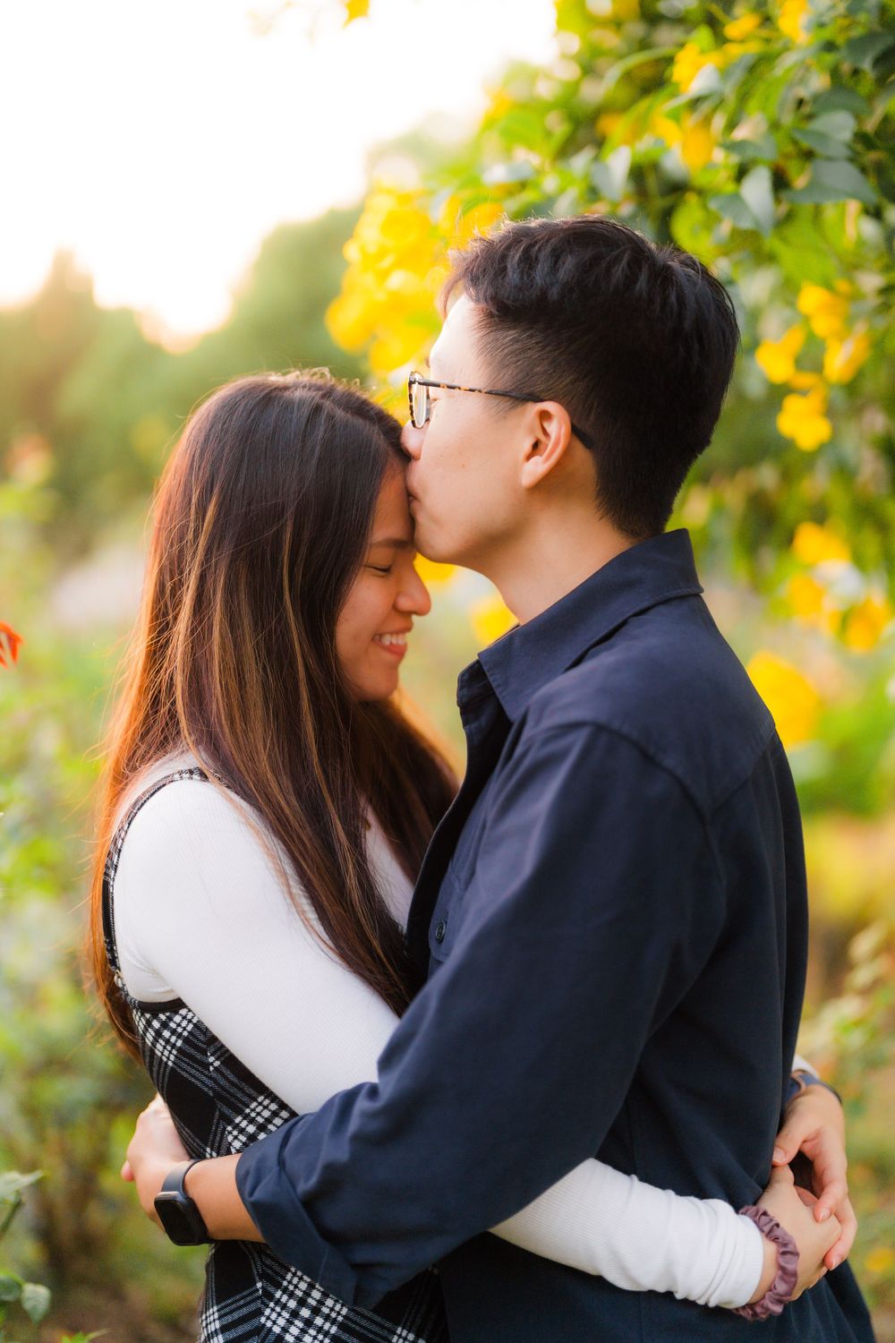 A romantic couple shares an intimate moment surrounded by yellow flowers in a garden at sunset.