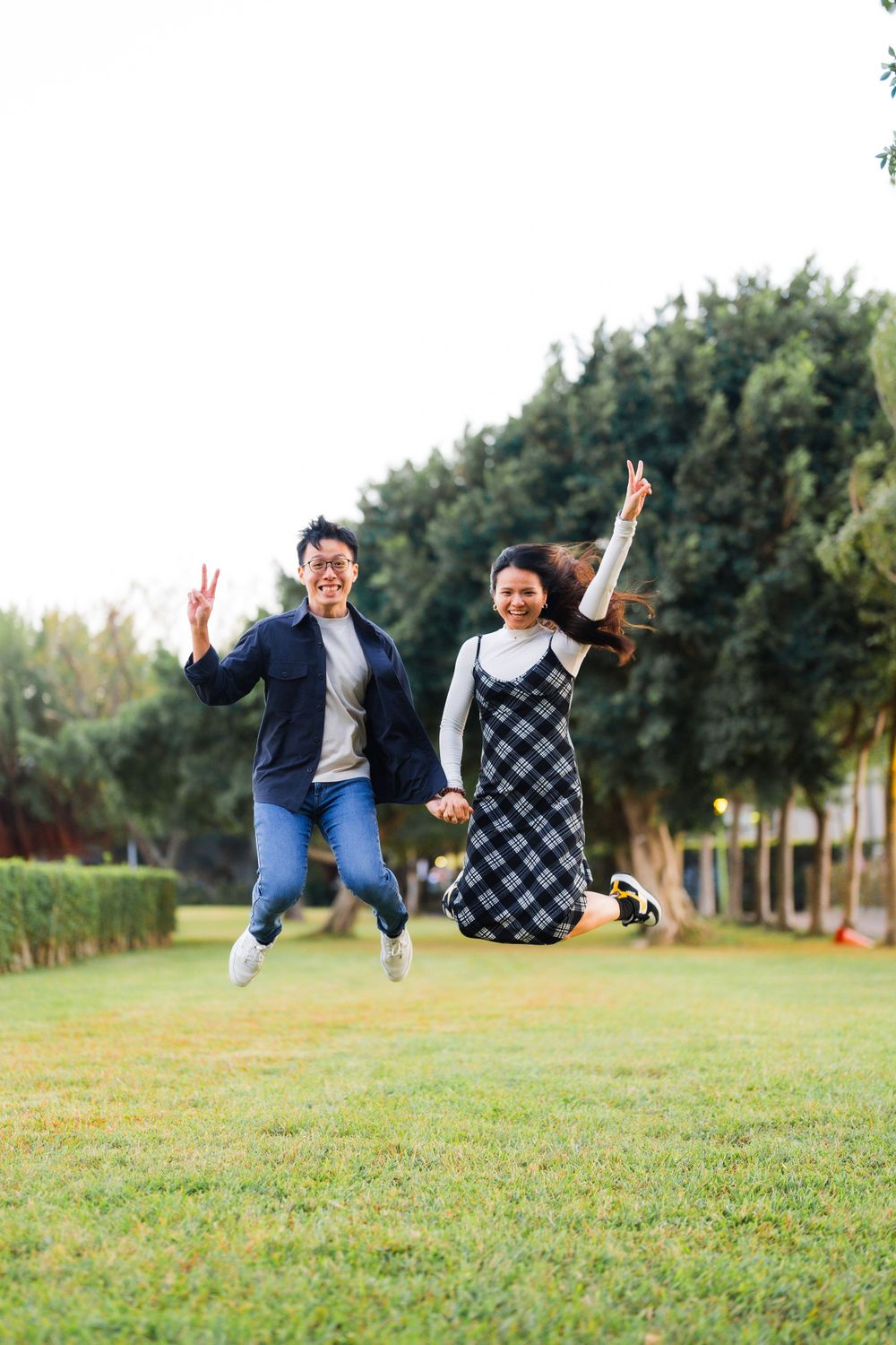 Joyful couple jumping together on grass in a park.