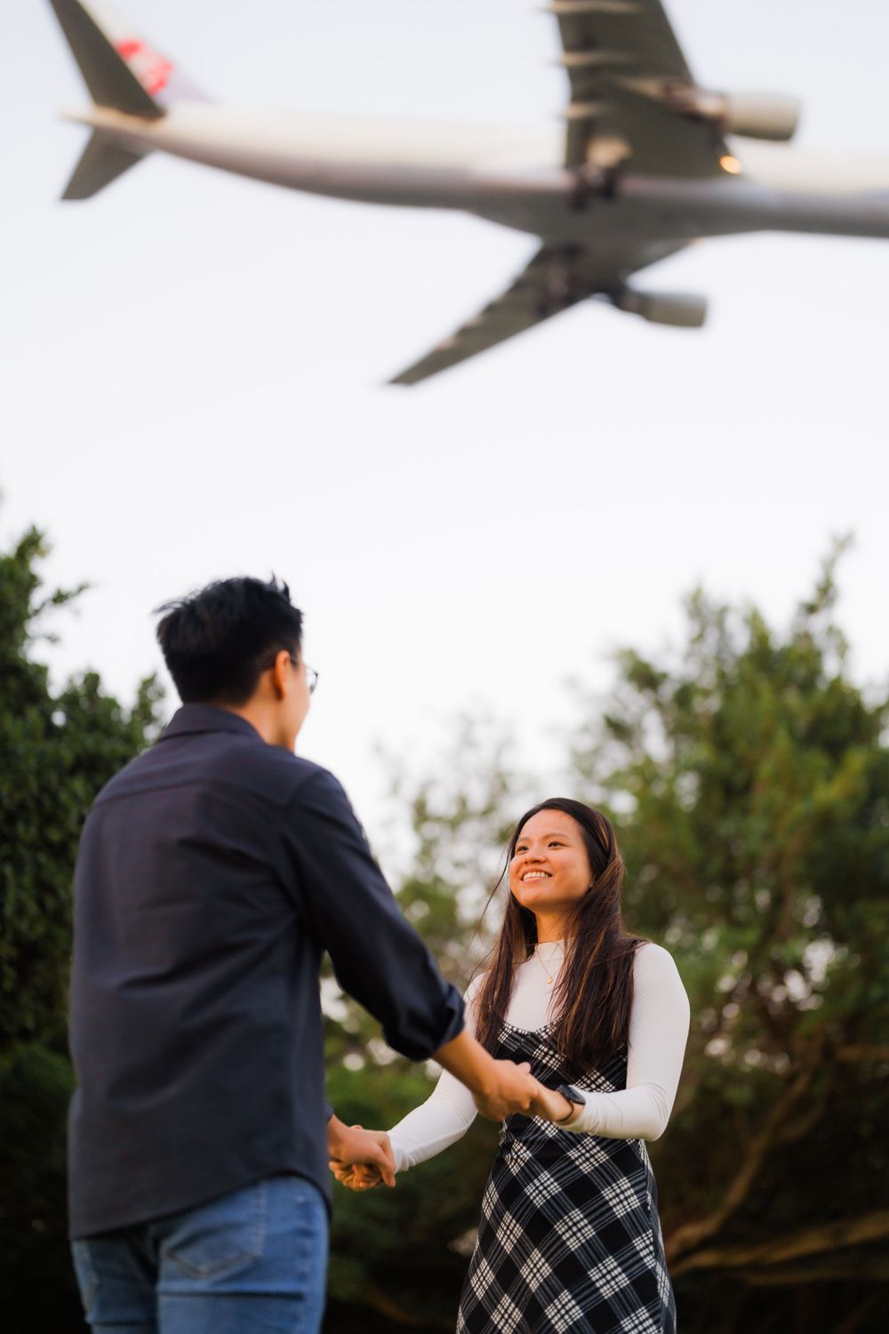 Couple sharing a moment while airplane flies overhead in park setting.