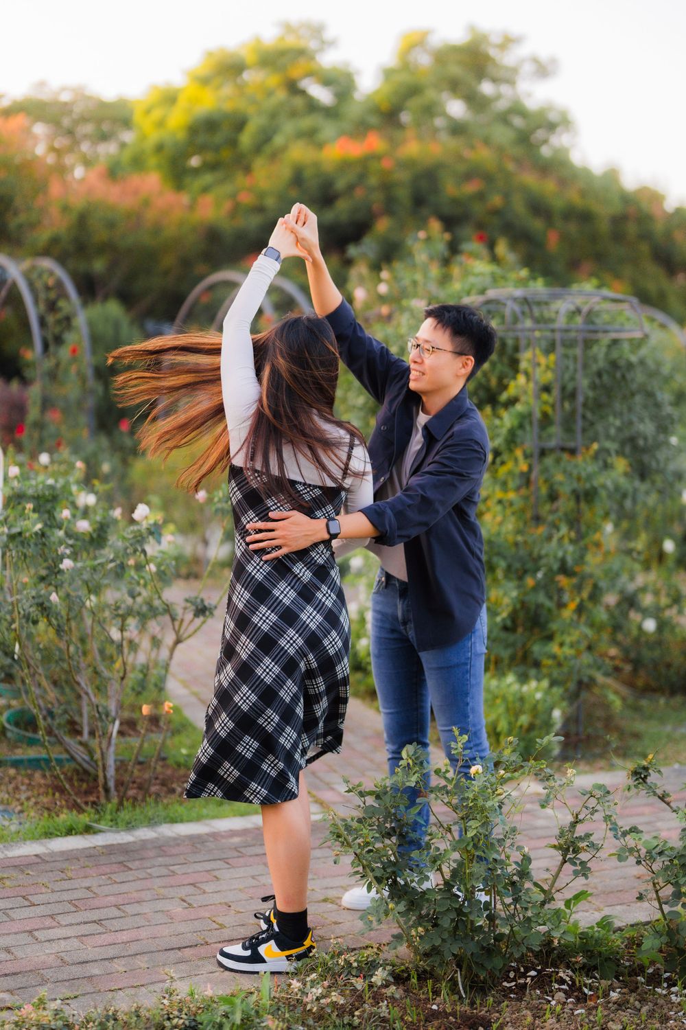 A couple dancing and twirling in a garden pathway surrounded by colorful flowers.