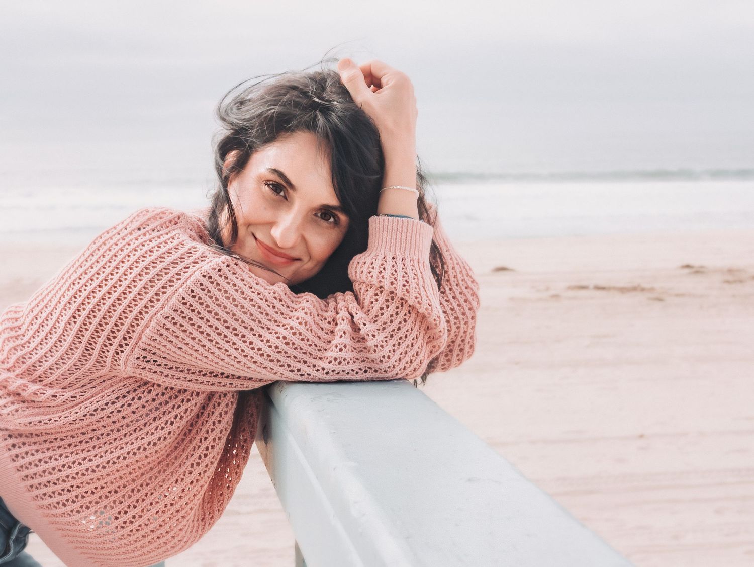 Casual beach portrait in pink sweater leaning on railing.