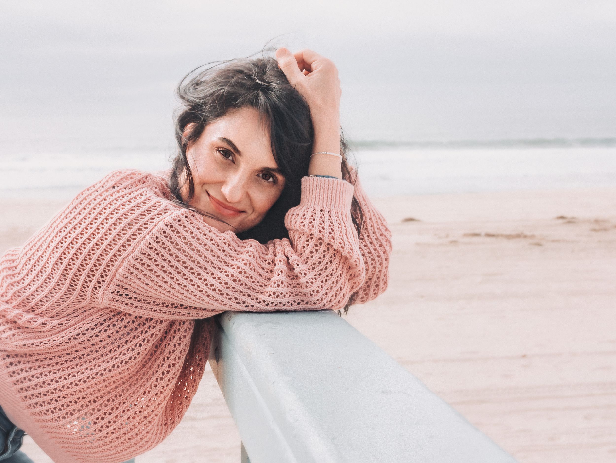 Casual beach portrait in pink sweater leaning on railing.