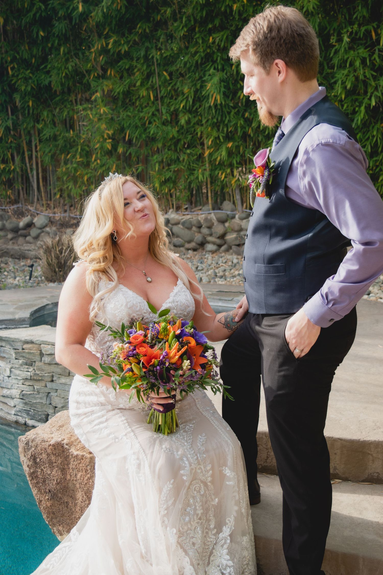 Couple in wedding attire sharing joyful moment by pool with bride holding colorful bouquet.