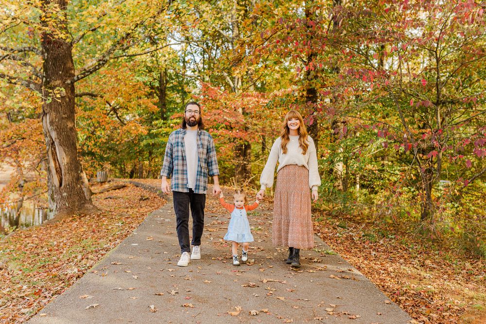 A family walking together on a path surrounded by vibrant autumn foliage.