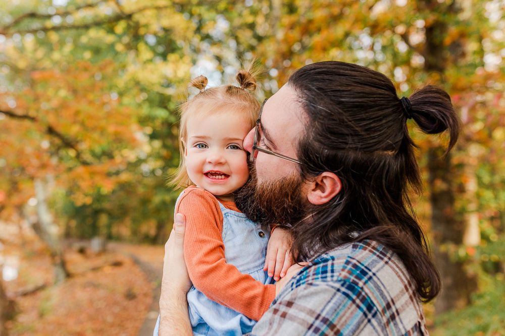 Father and toddler sharing a tender moment among autumn foliage.
