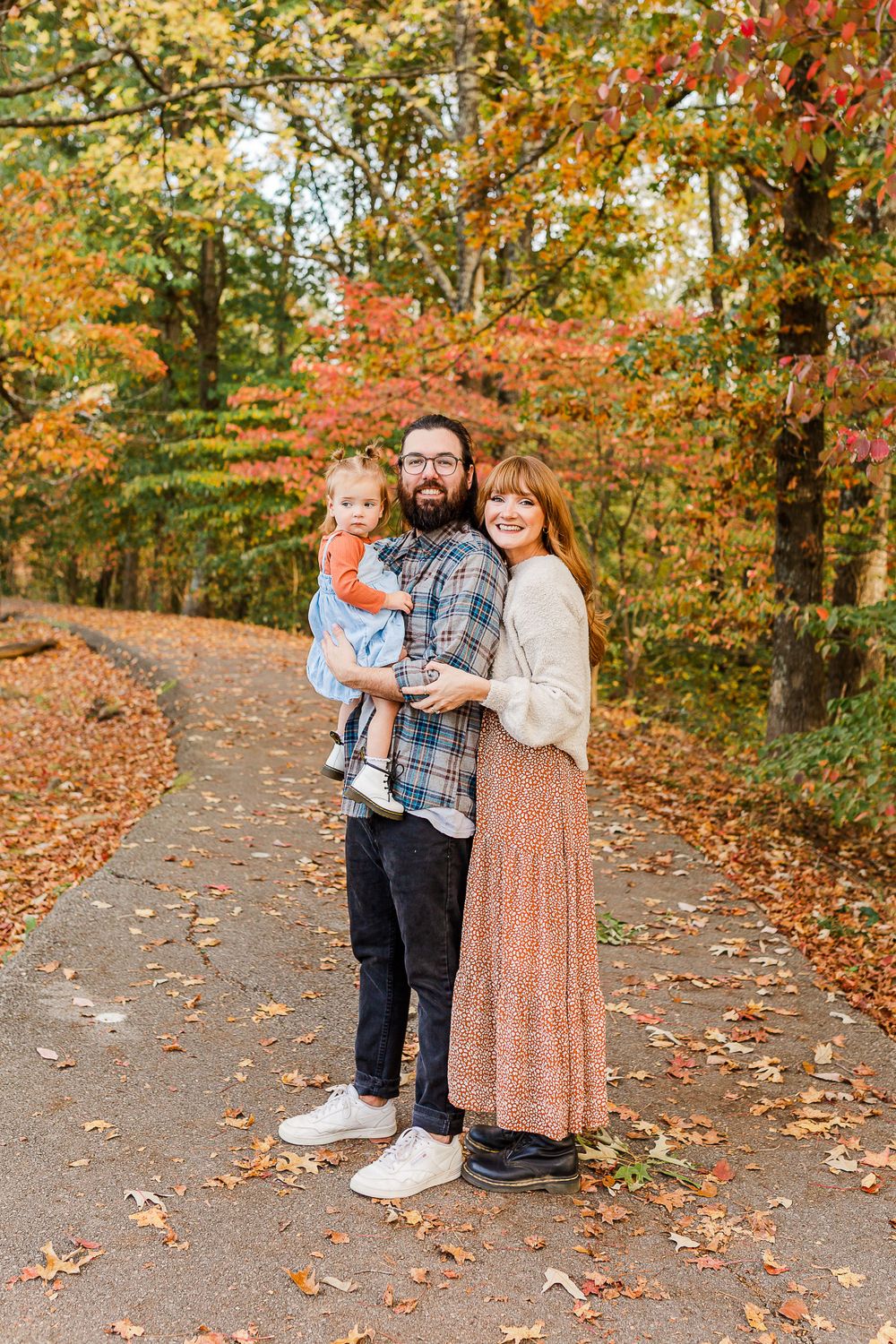 A family portrait on a path with vibrant fall foliage in the background.