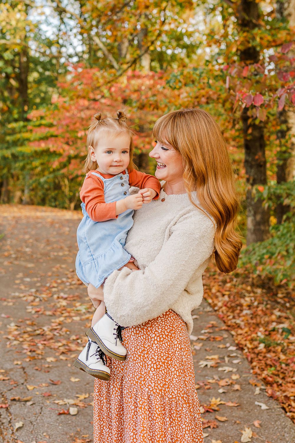 Parent and toddler share joyful moment on autumn path surrounded by colorful trees.