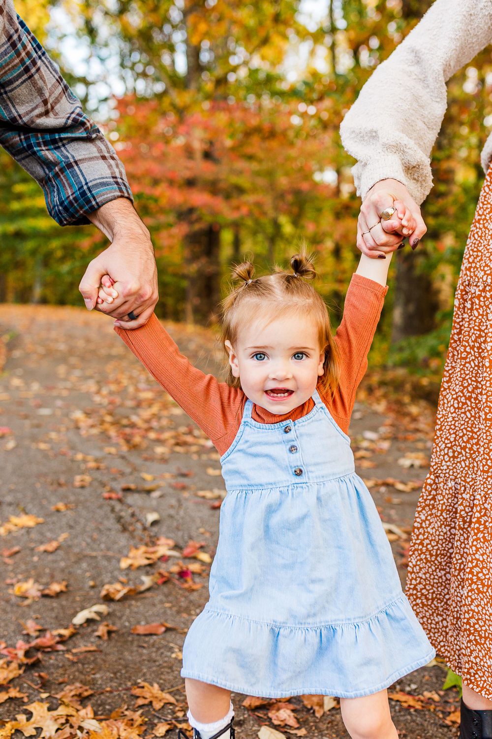 A joyful moment with raised hands and bright smiles on a leaf-covered autumn path.