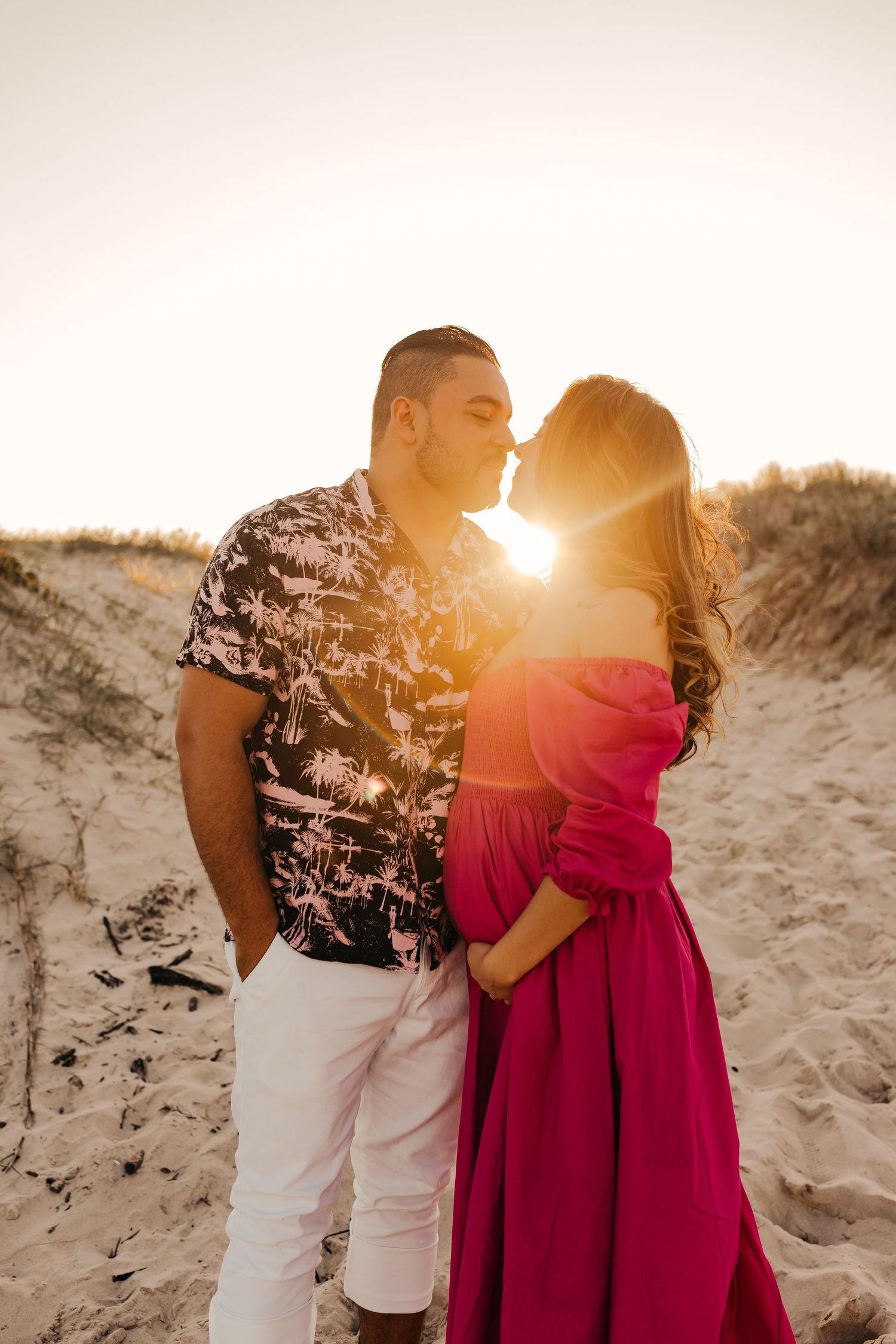 Intimate sunset moment between couple on sandy dunes with golden light.