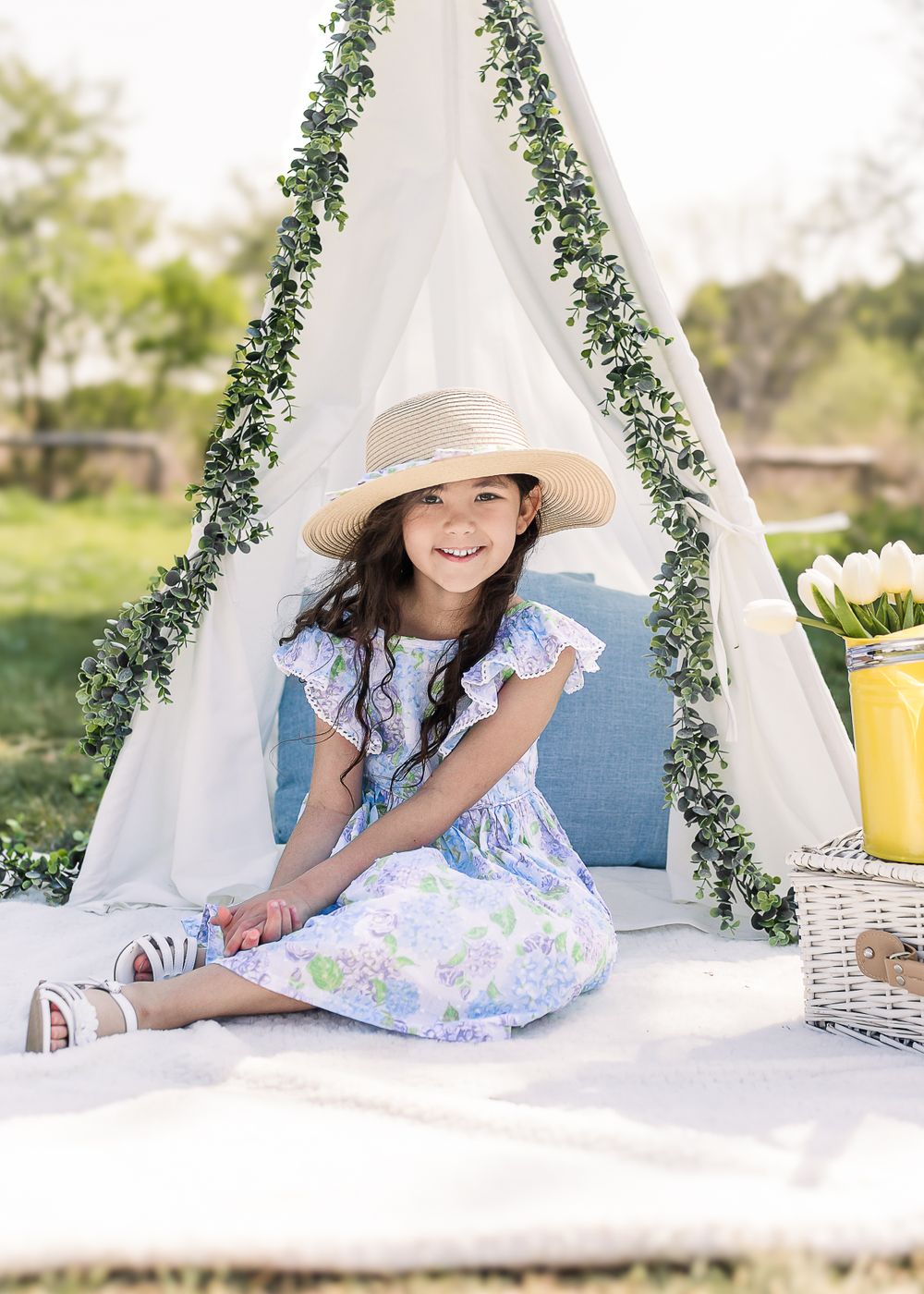 White teepee tent decorated with greenery and flowers creates dreamy outdoor photo setting.