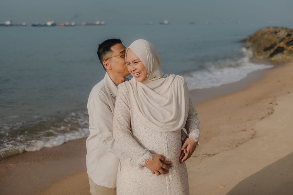 Couple in matching cream outfits sharing a romantic embrace on a sandy beach at dusk.