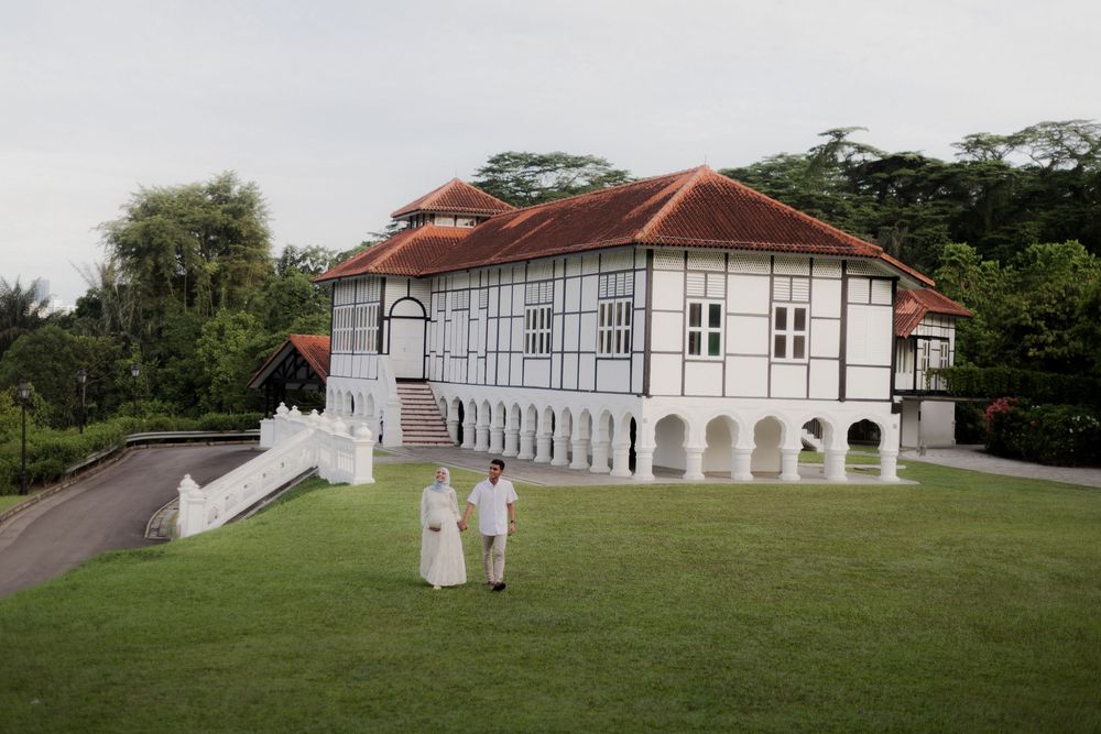 Two people walking on green lawn before a white colonial building with red roof surrounded by lush trees.