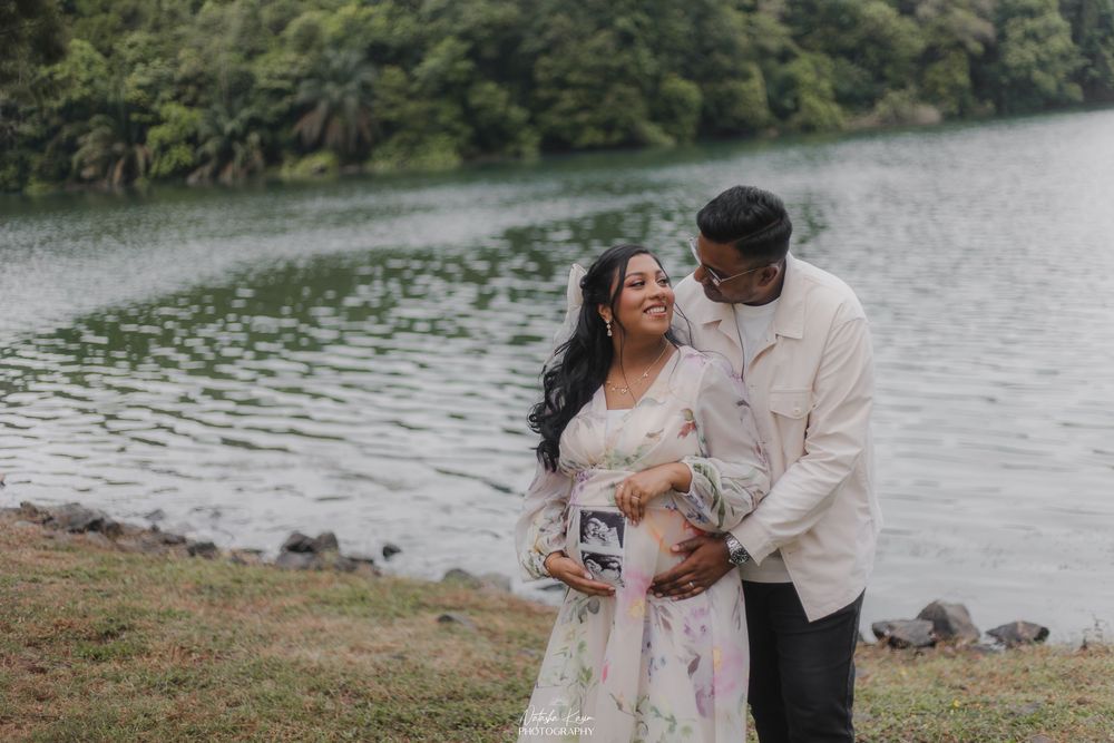 Couple sharing a tender maternity photo shoot by a serene lake, holding ultrasound pictures outdoors.