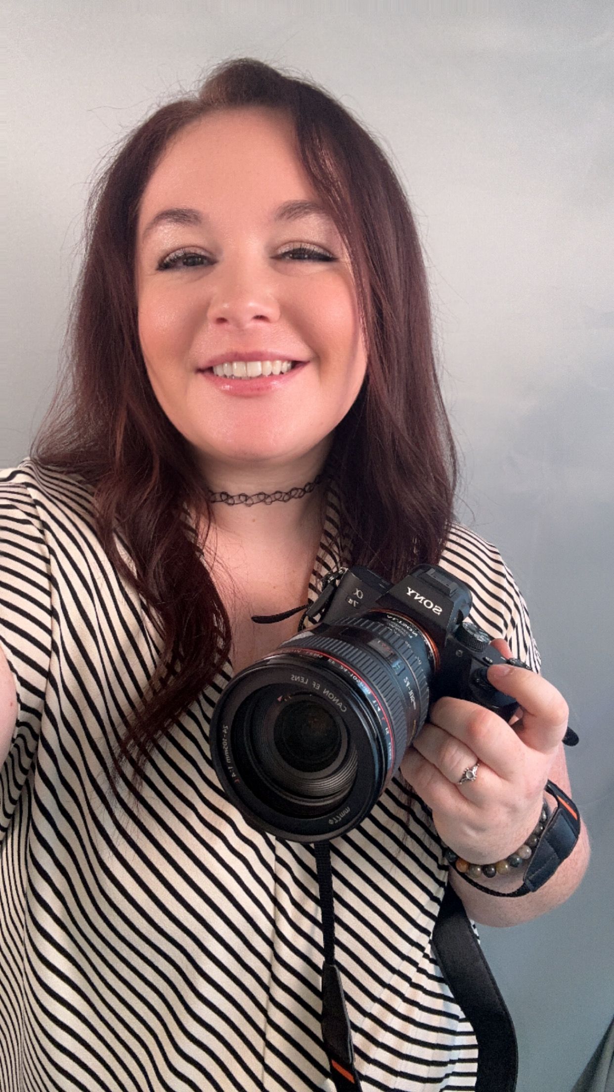 Person holding professional camera equipment in striped shirt.