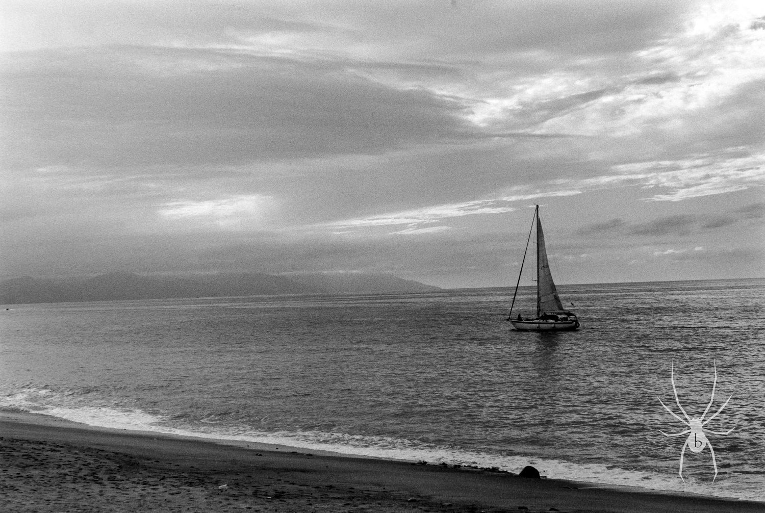 Black and white seascape with a lone sailboat on the horizon under cloudy skies.