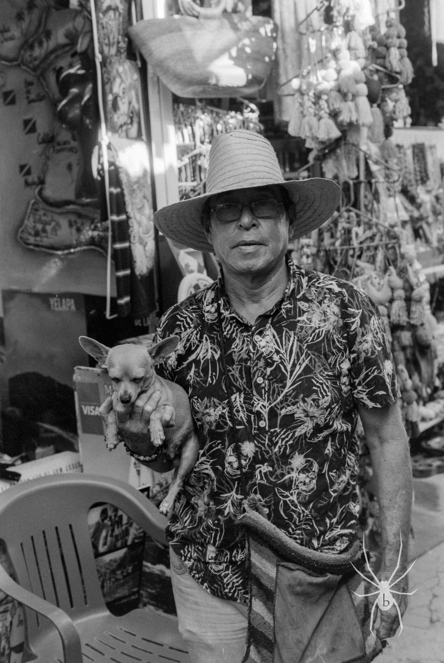 Black and white portrait of someone holding a small dog at a market.