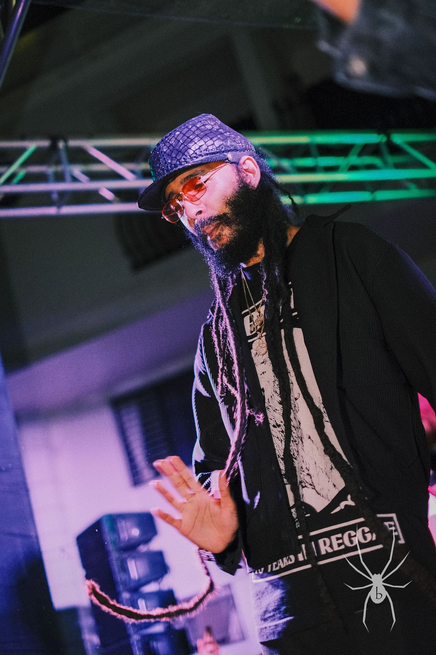 Concert performer in purple hat and black jacket under neon stage lights.