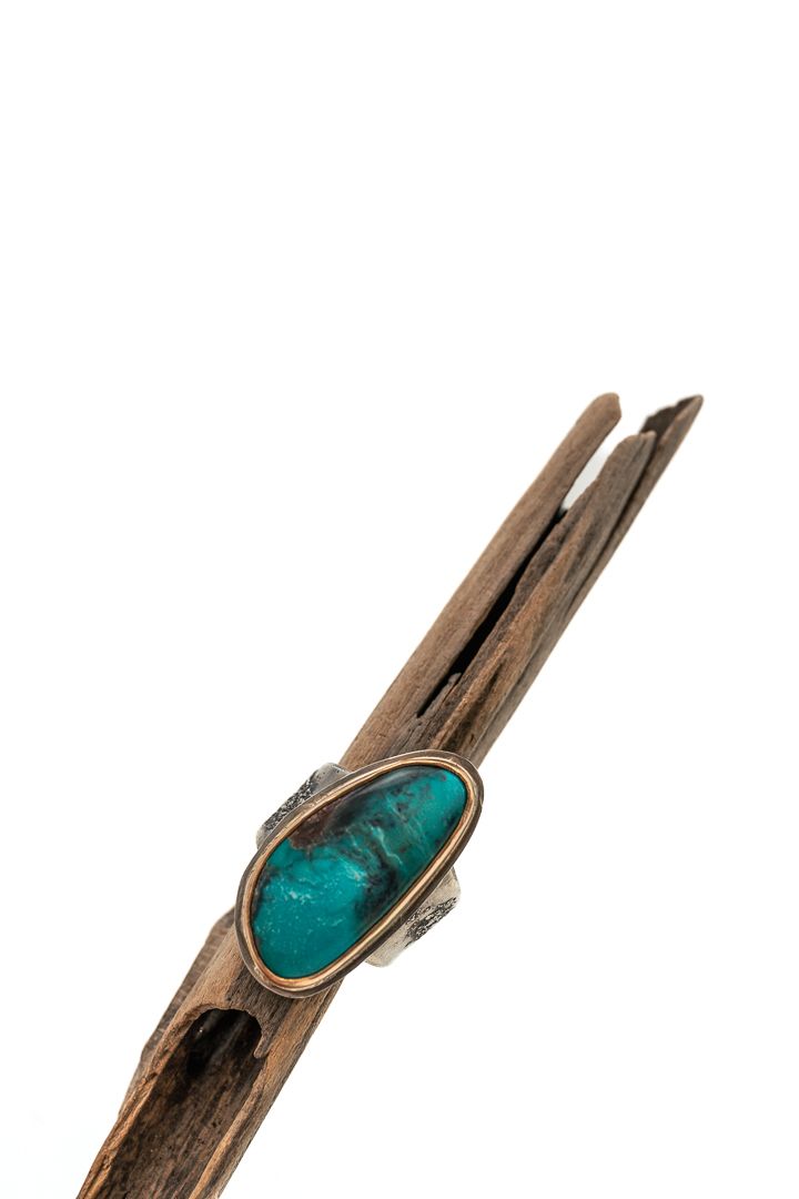 Vintage wooden branch adorned with turquoise gemstone ring against white background.