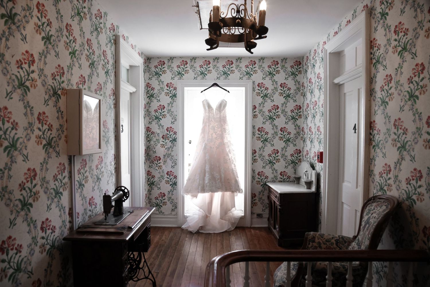 Vintage room with floral wallpaper and wedding dress illuminated in window.