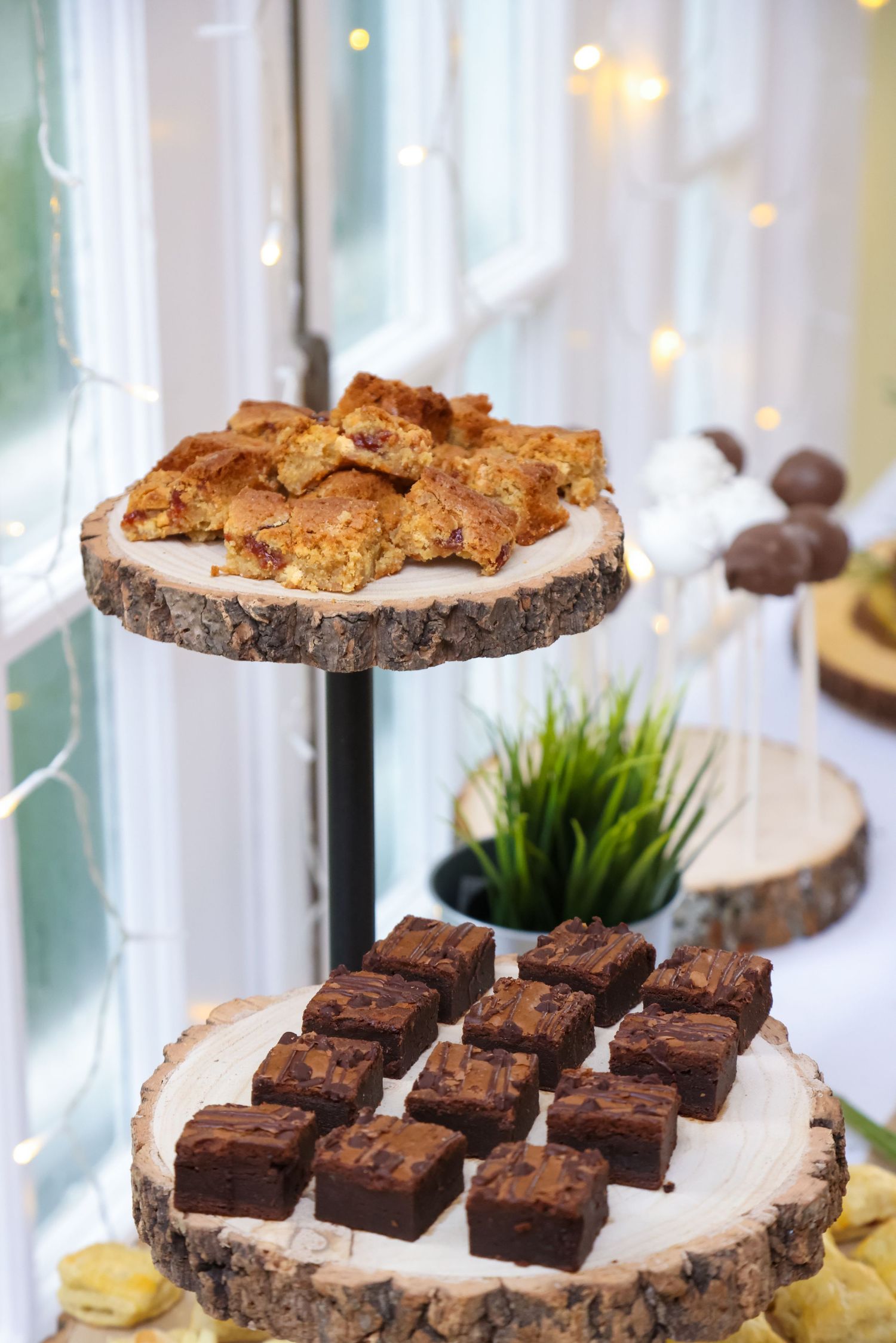 Two-tiered rustic dessert display with brownies and pastries on wood slice stands.