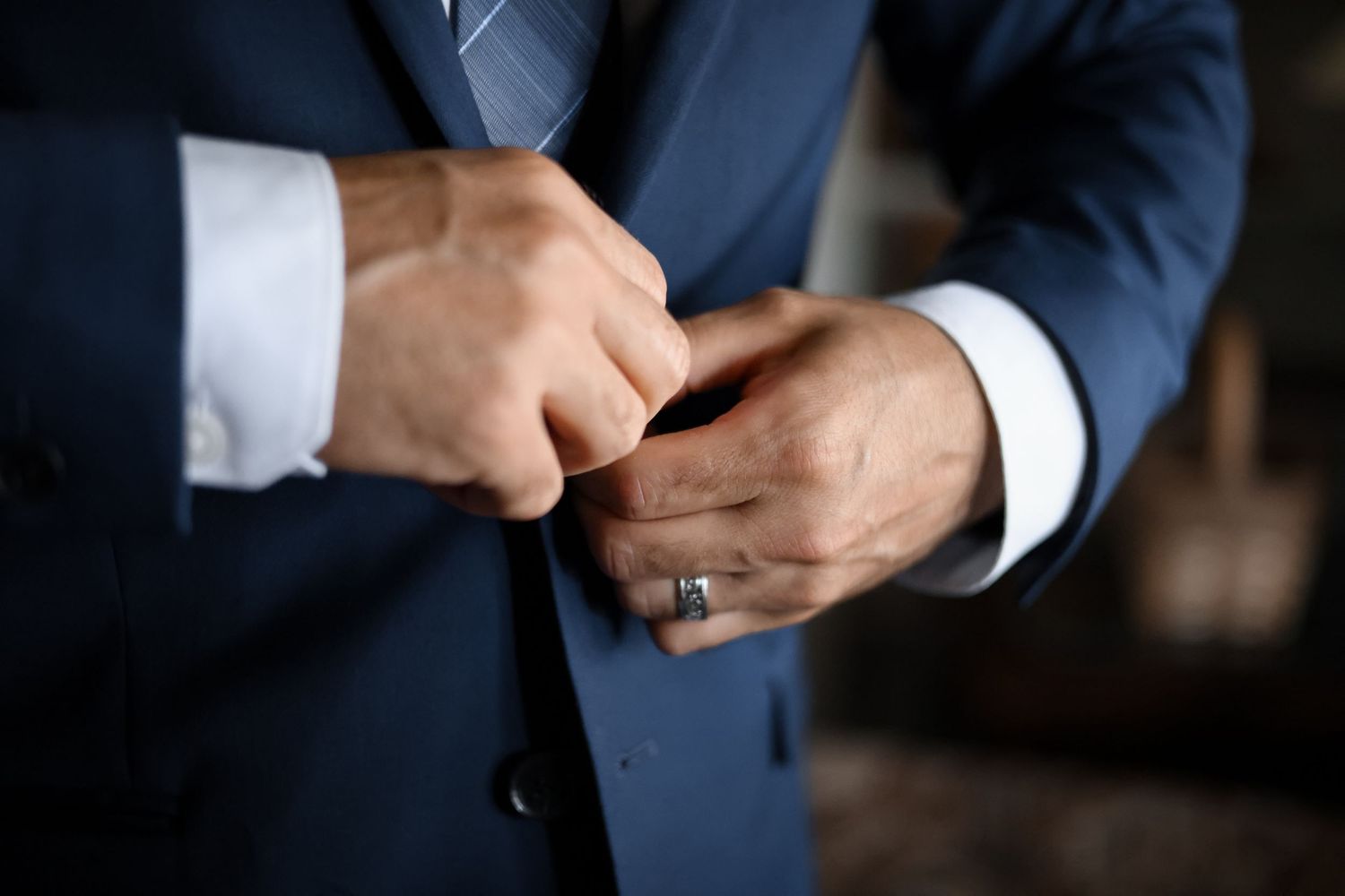 Close-up of a groom adjusting his sleeve and cuff links while wearing a navy blue suit.