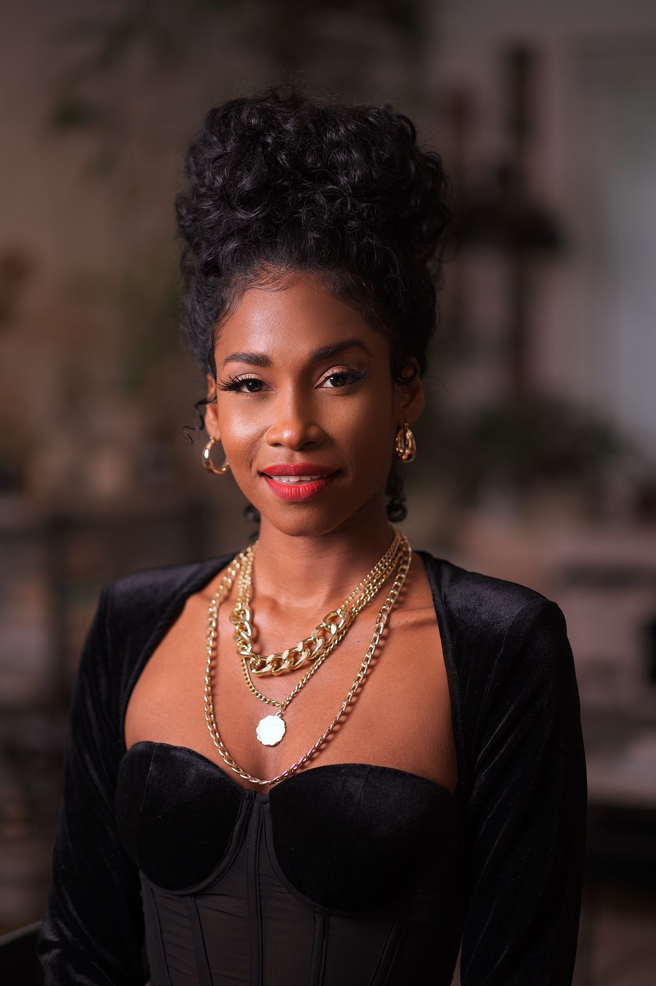 Elegant portrait featuring gold chain necklaces and black velvet blazer in professional setting.