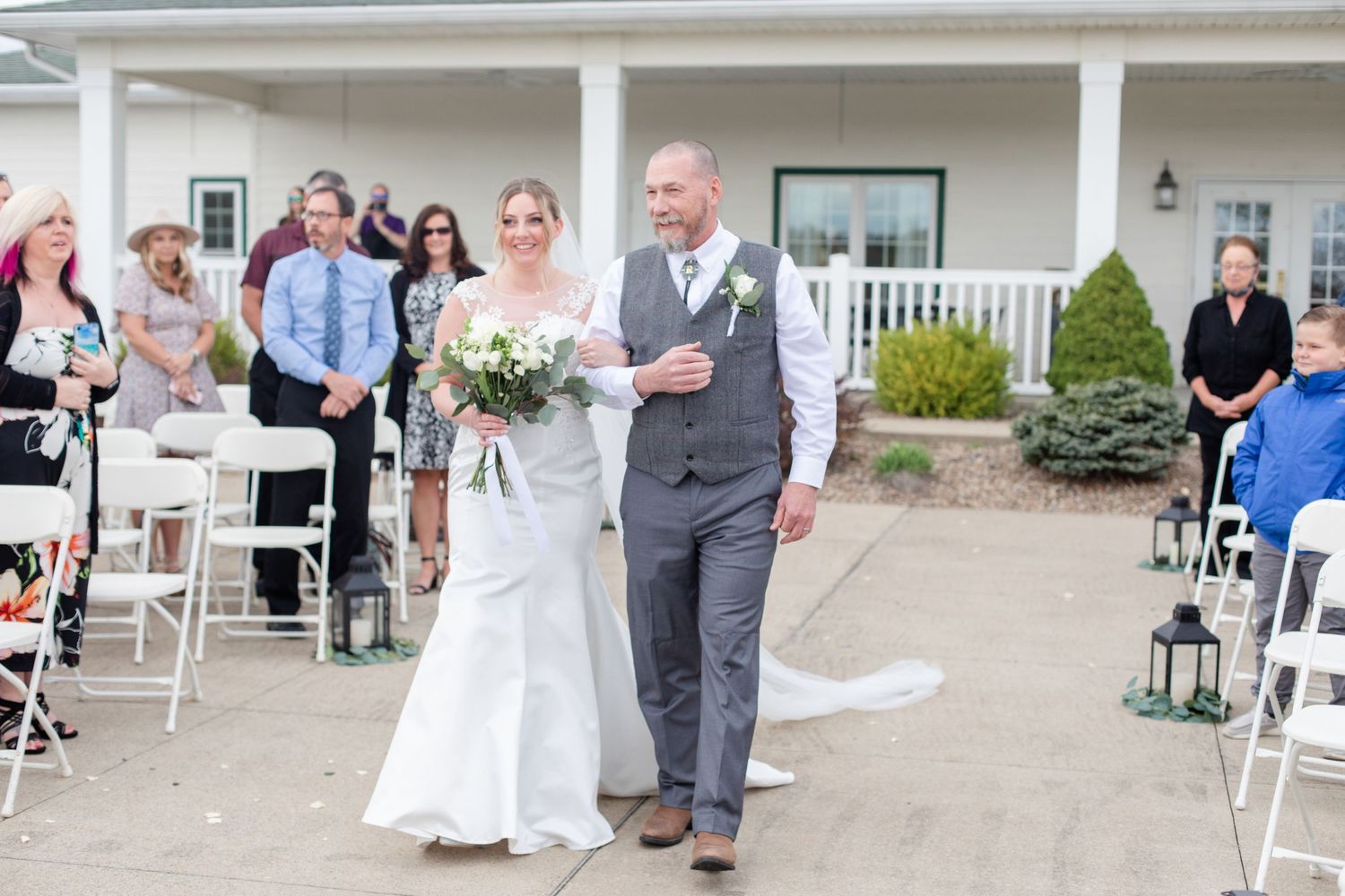 Outdoor wedding ceremony setup with white chairs and decorative arrangements at a venue with white columns.