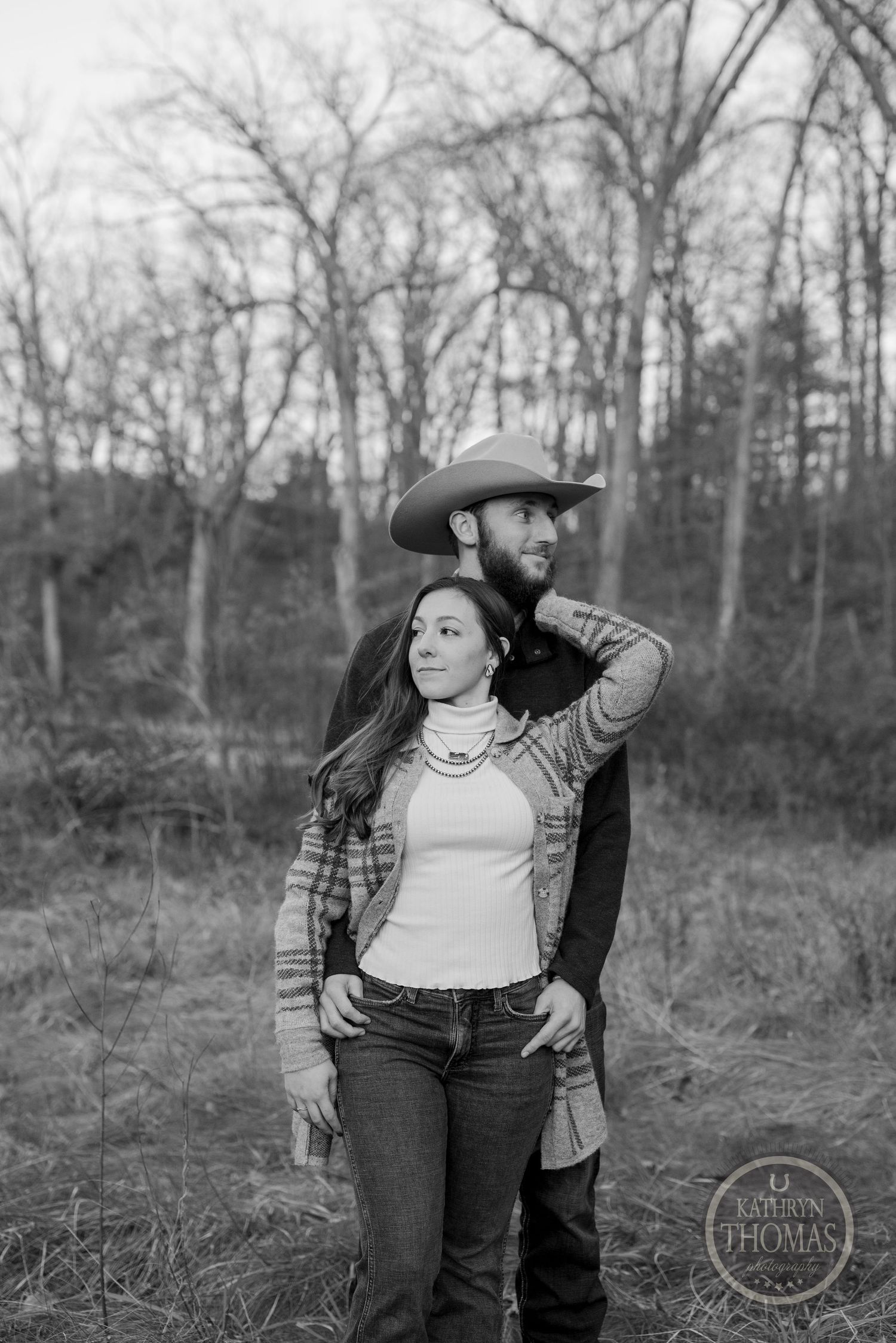 A black and white portrait of a couple in western style clothing in a natural setting.