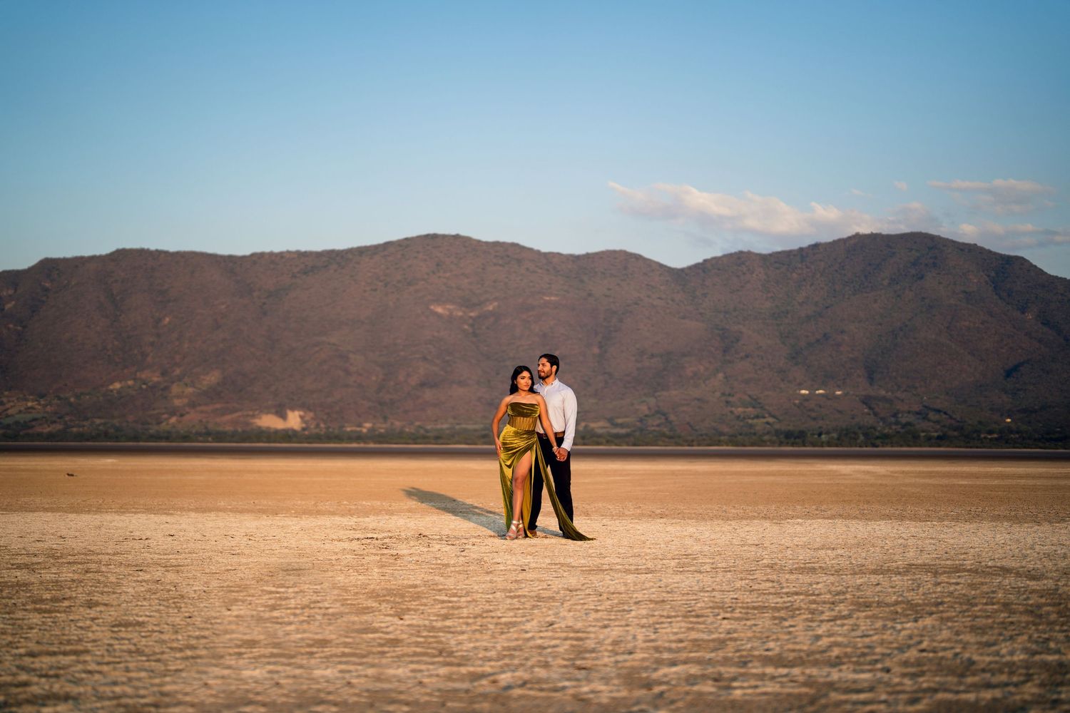 Wide panoramic desert landscape with distant mountains and figures in the dry lakebed.