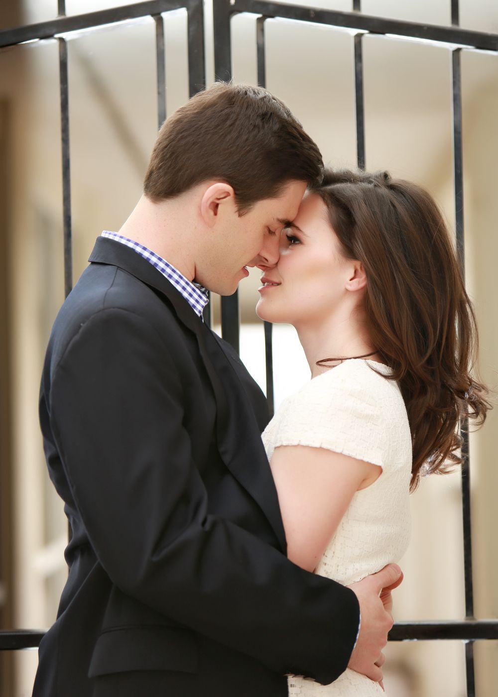 A romantic couple embracing and sharing an intimate moment against metal railings.