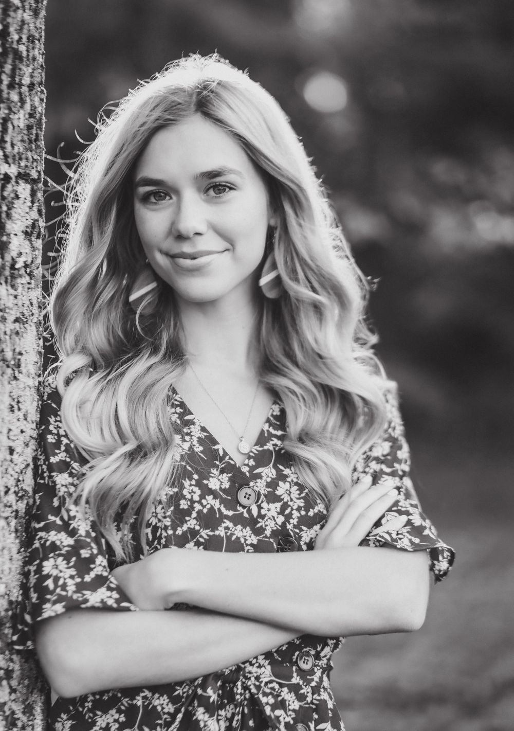 Black and white portrait of woman with flowing blonde hair leaning against tree.
