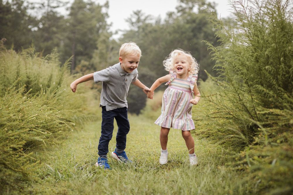 Two children playing and running together through tall grass in a summer field.