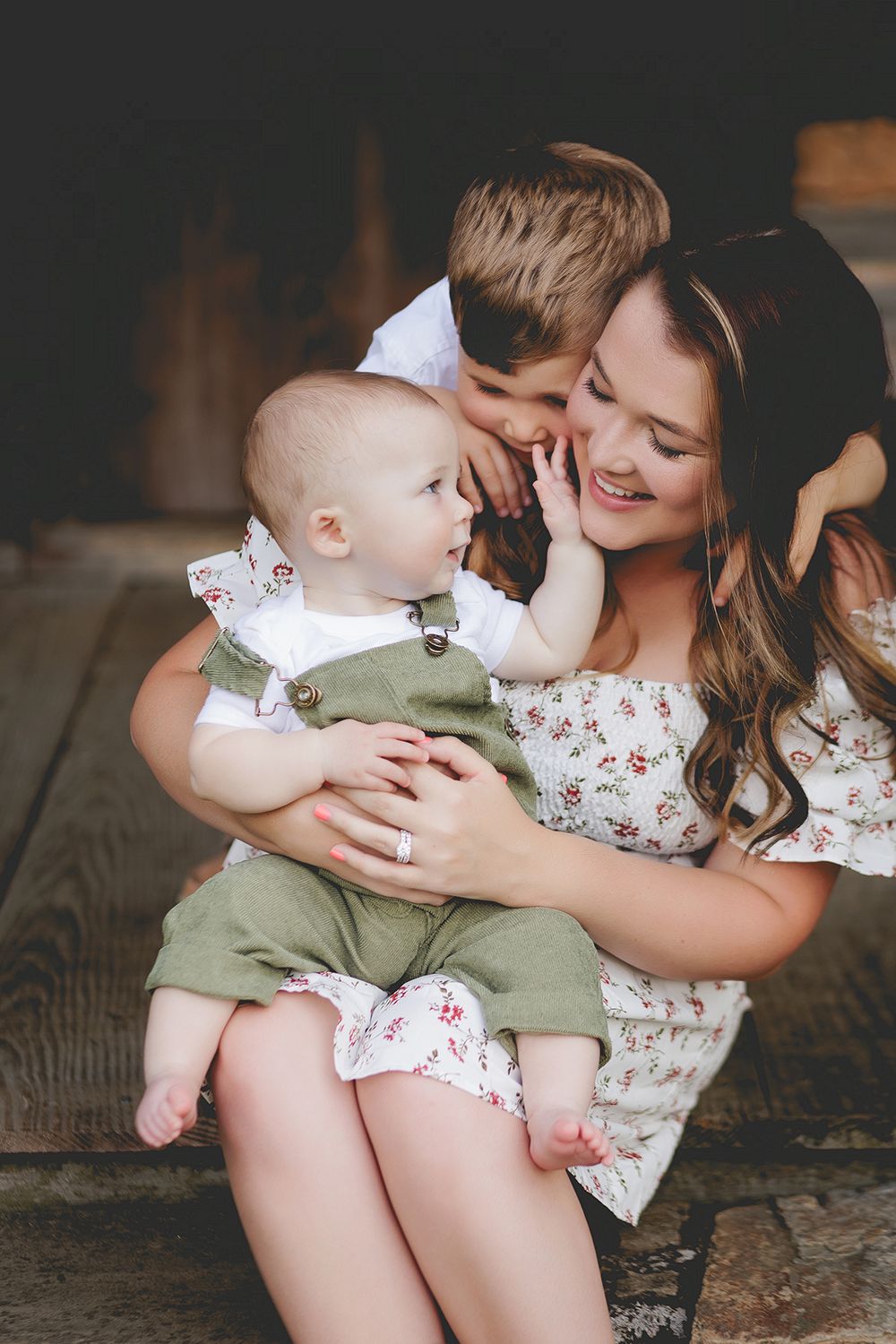 A tender family moment as a baby in green overalls shares affection with loved ones in a rustic setting.