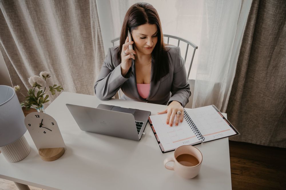 Professional woman multitasking on phone while reviewing notes on laptop at desk.