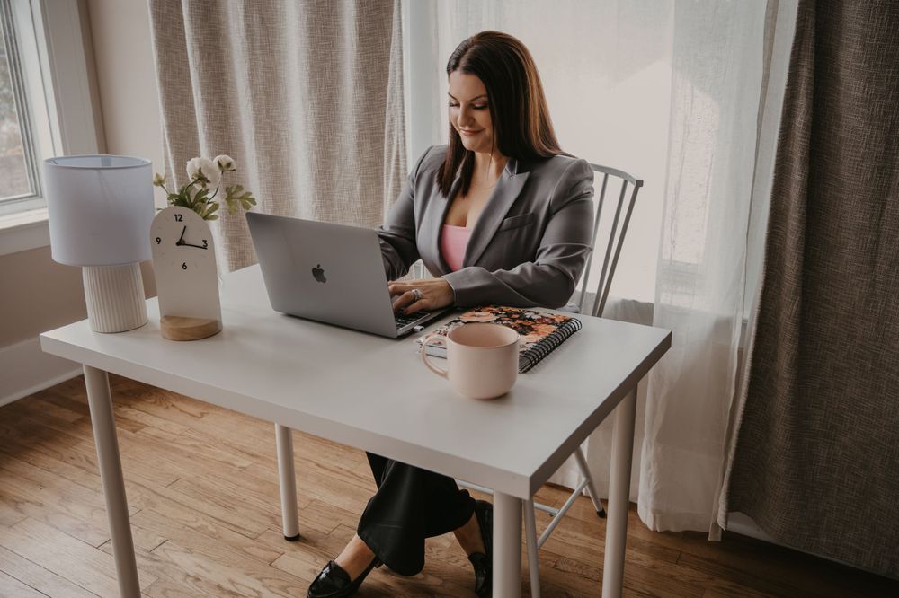 Smiling businesswoman typing on MacBook laptop at modern white home office desk.